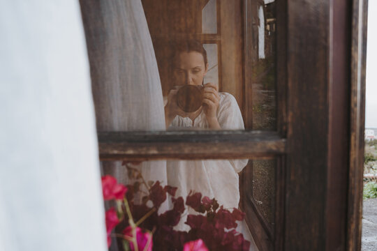Woman taking a photo through a window frame with flowers