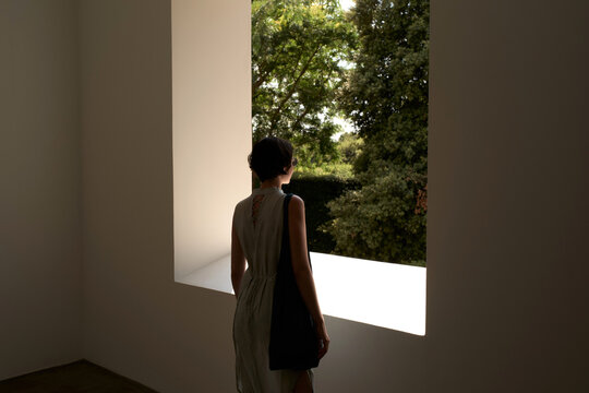 Woman Looks out of a Large Window at Trees Outside