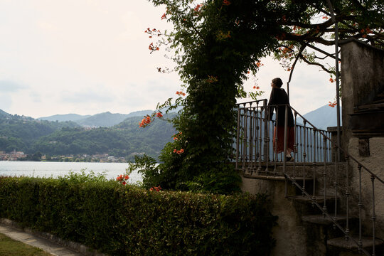 Woman Stands on Balcony Overlooking Lake and Mountains