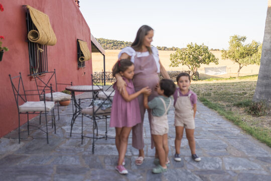 Happy pregnant mother hugging her three children outdoor at home