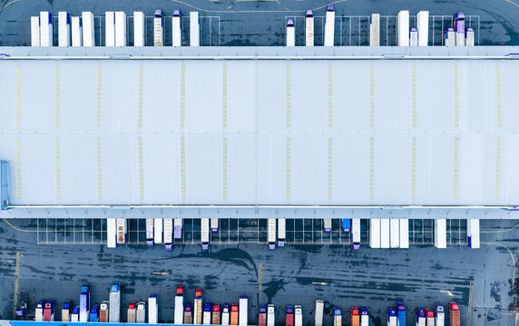 Aerial top view of logistics warehouse with solar rooftops and trucks