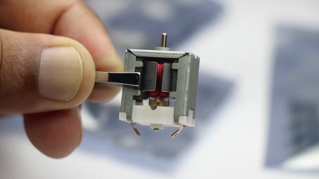 Open metal frame brushed dc motor with visible internal components held by the tweezers