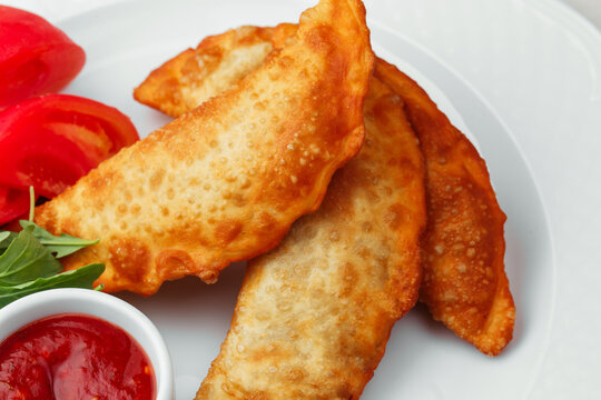 Golden fried chebureki stuffed meat pastries with tomato sauce and fresh garnish, traditional savory food