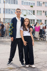 Fototapeta premium A boy and a girl pose together outdoors, dressed in smart casual attire, exuding a playful and cheerful mood.