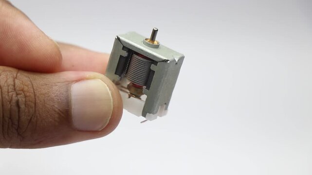 Mini dc motor with visible internal parts including the rotor and shaft held in hand close-up macro shot