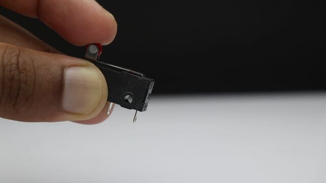 Limit switch electromechanical component held in fingers showing the small lever and metal pin that trips when pressed against an object