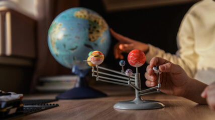 Fototapeta premium Child's hands exploring a solar system model next to a globe