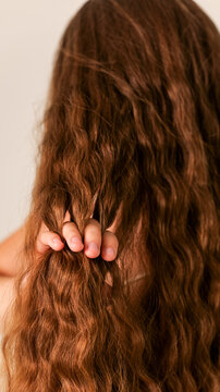 Close-up of a person's hand gently holding a strand of long, wavy brown hair
