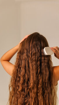 Woman brushing her long wavy brown hair with a white brush