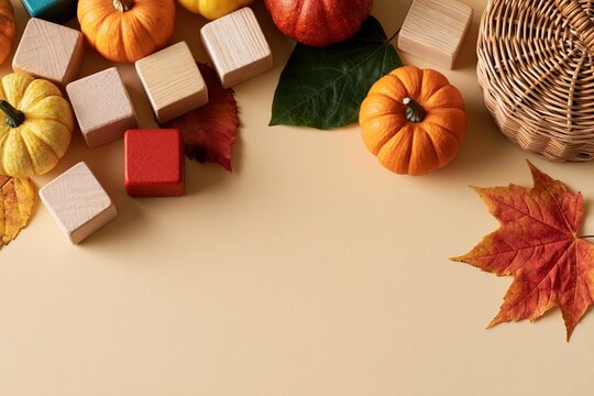 Miniature pumpkins and wooden blocks with autumn leaves and wicker basket on cream tabletop