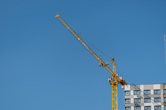 Tall yellow construction crane reaching into a clear blue sky near a modern building under development in the bustling city
