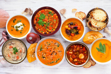 Fototapeta na wymiar Selection of delicious homemade warm and cozy autumn soups. Above view table scene on a white wood background. Pumpkin, squash, sweet potato, mushroom, French onion and hearty vegetable.