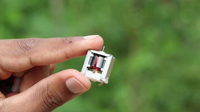 Hand holding small dc motor with minimal frame showing visible internal parts