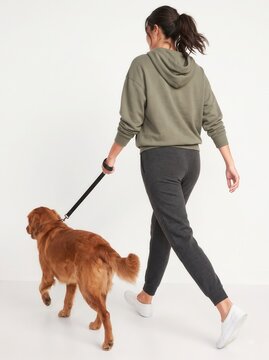 Rear view of a woman in gray casual loungewear walking her fluffy dog on a leash, isolated on white background.-1