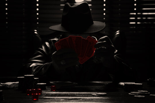 Mafia. Man playing cards at wooden table in dark room