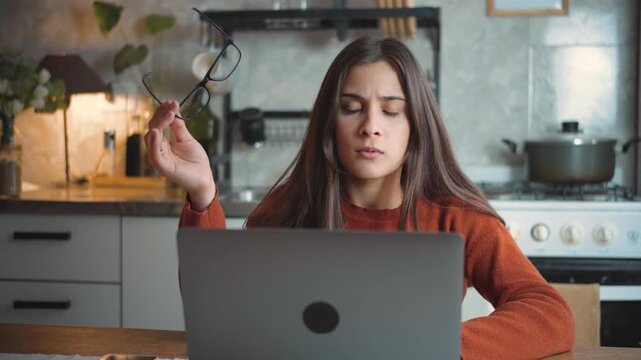 Young Latina woman using her laptop at home and looking at the camera with intense frustration, highlighting stress, technology problems, and digital challenges.
