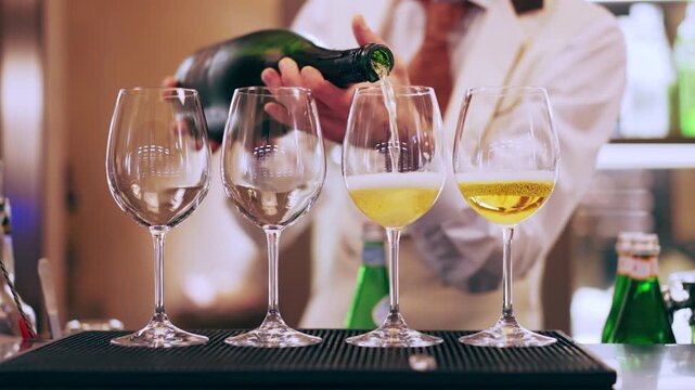 Transparent glasses on bar counter, male bartender in uniform pouring fizzing refreshing Prosecco or Champagne into the goblets to make refreshing cocktails