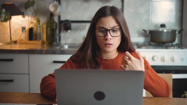 Young Latina woman sitting at home using her laptop while looking at the camera with intense frustration and anger, highlighting stress, technology problems, and emotional tension.
