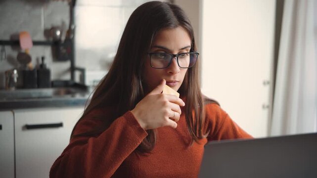 Happy Hispanic woman shopping online at home with her laptop while affectionately kissing her credit card, highlighting ecommerce, purchases, consumer excitement, and digital shopping.
