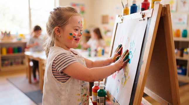 Young girl with Down syndrome happily painting with colorful handprints at art class