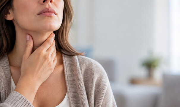 Woman touching her throat with hand feeling pain while sitting at home. Sore throat, tonsillitis and cold symptoms. Flu infection and angina treatment concept. Health care and medicine