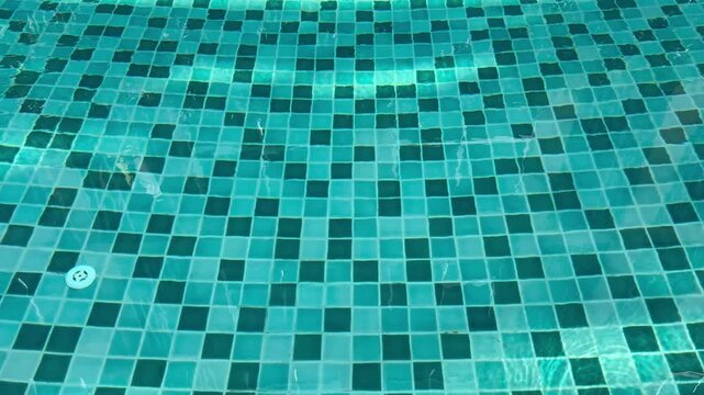 Static overhead shot of gentle ripples on blue mosaic swimming pool water.