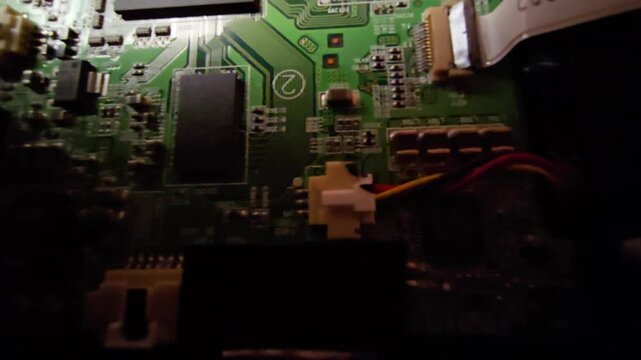 Top down macro video revealing a green circuit board with microchips, copper traces, and wiring connectors from shadow, ideal for tech and cyber B-roll.
