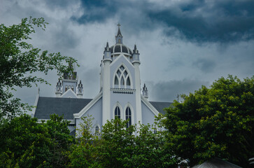 Obraz premium Roman Catholic Gothic Church with Tall Steeple and Arched Windows Under Stormy Sky
