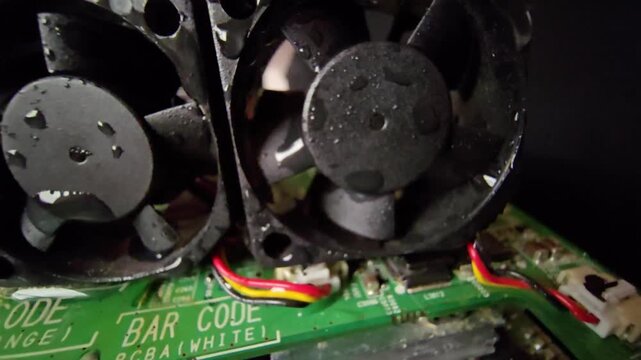 Extreme close-up macro view of wet cooling fans with water droplets on a green electronic circuit board.