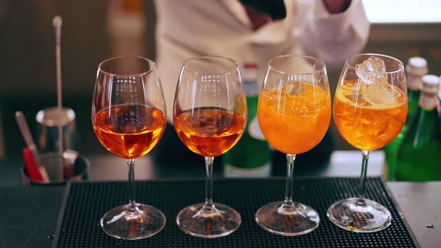 Bartender adding ice cubes into the glasses with Prosecco and Aperol Spritz, preparing of refreshing drinks at the bar counter, fizzing beverage for celebration party