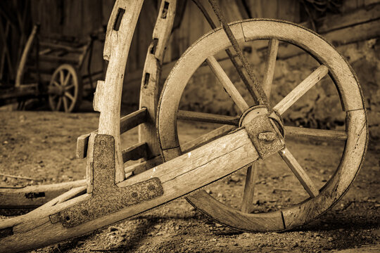 Vintage wooden cart with large wheels resting on a dusty floor in a rustic barn environment during the late afternoon light