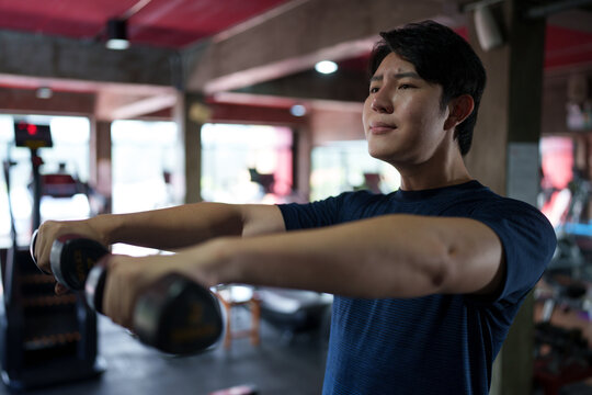 Young Asian man performing arm stretching exercise during fitness training session at modern gym interior