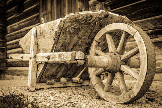Vintage wooden cart with large wheels resting on a dusty floor in a rustic barn environment during the late afternoon light