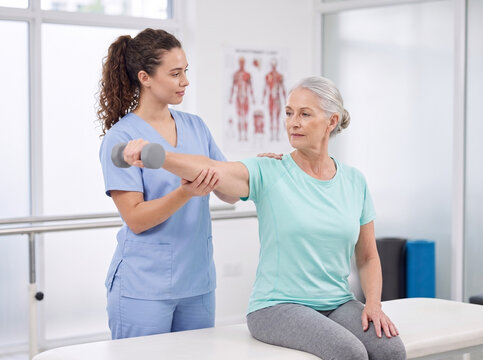young female physiotherapist assisting senior woman during seated single arm dumbbell lateral raise in clinic