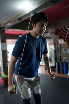 Young Asian man training with jump rope in modern fitness center during indoor cardio workout