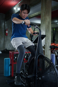 Young Asian male athlete performing intense air bike cardio workout in underground gym training facility