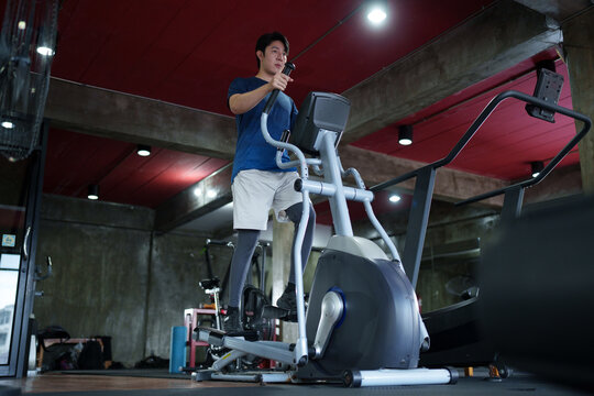 Young Asian man using elliptical cross trainer machine during cardio workout in modern industrial fitness center