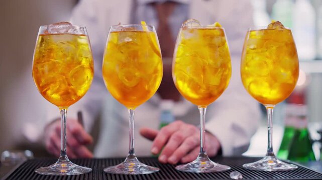 Bartender adding orange fruit pieces to Aperol Spritz cocktail at the bar counter, process of preparation of refreshing drink for guests aperitif