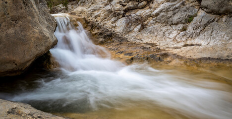 A beautiful small waterfall cascades smoothly over rocks through a narrow rocky canyon. © @CMG_IG