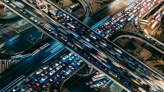 Aerial long exposure time lapse of busy city highway interchange at night with blurred car headlights and taillights moving through urban traffic junction.