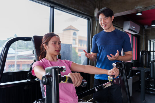 Young Asian fitness trainer instructing woman on cable machine exercise technique in modern gym