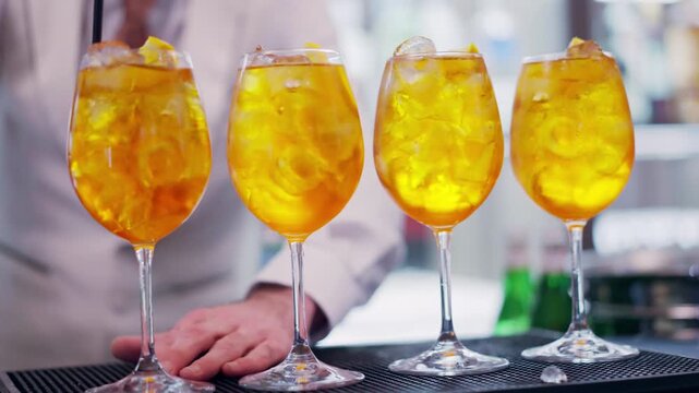 Bartender adding drinking straws into the goblets with prepared Aperol Spritz cocktail at the bar counter, alcoholic refreshing drink for guests