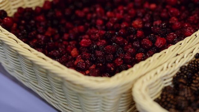 Dried red berries and rosehips in woven basket at market stall. Close-up of healthy dried fruits and berries for herbal tea and natural medicine concept.