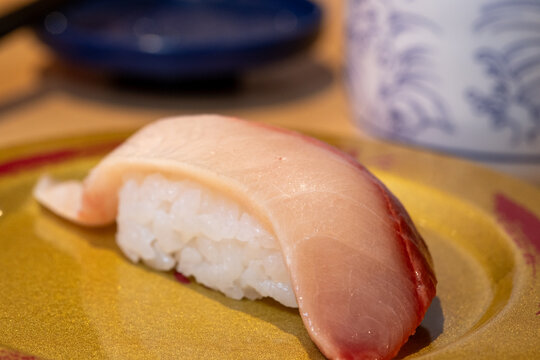 Close-up shot of fresh yellowtail belly (hamachi) nigiri sushi on a gold ceramic plate.