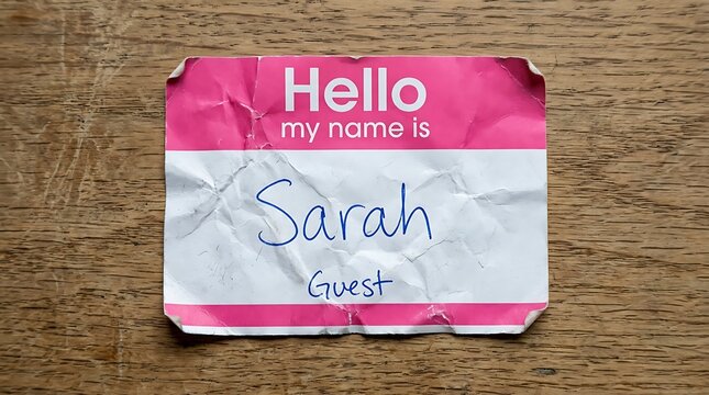Wrinkled pink hello my name is sticker tag on a wooden surface with identity