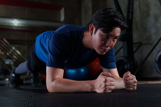 Young Asian man doing plank exercise on mat in modern gym training for core strength and endurance