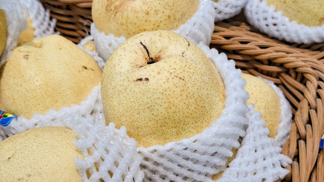 Fresh Chinese Nashi Pears Wrapped in White Foam Netting Displayed in Wicker Basket at Grocery Supermarket Shelf
