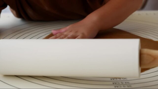 Close-up of child rolling gingerbread dough with rolling pin for homemade Christmas Cookies.