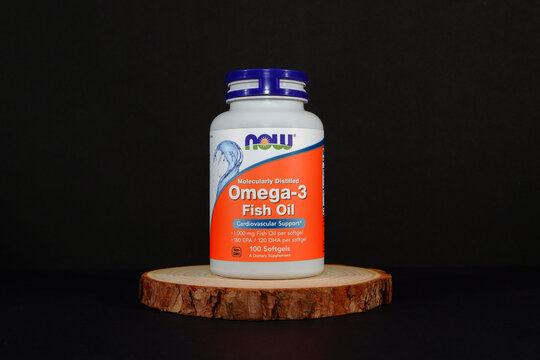 NOW Omega-3 Fish Oil 100 Softgels Bottle on Wooden Slice - Black Background Product Shot