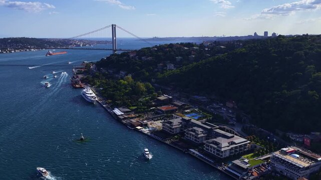 Aerial cityscape of Istanbul Bosphorus shoreline featuring waterfront estates, boats, deep blue sea, and green hills under clear sky